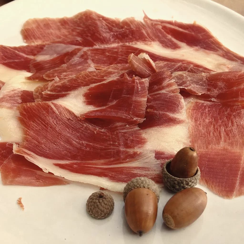 Slices of Iberian bellota ham with marbled fat beside a few acorns