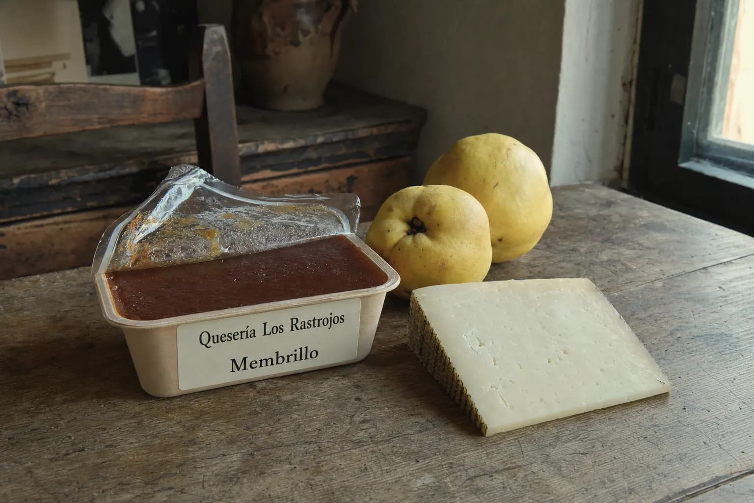 Tub of Quesería Los Rastrojos quince paste beside cheese and quinces in a kitchen