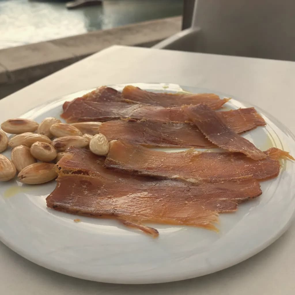Thin slices of mojama with olive oil and almonds on a plate