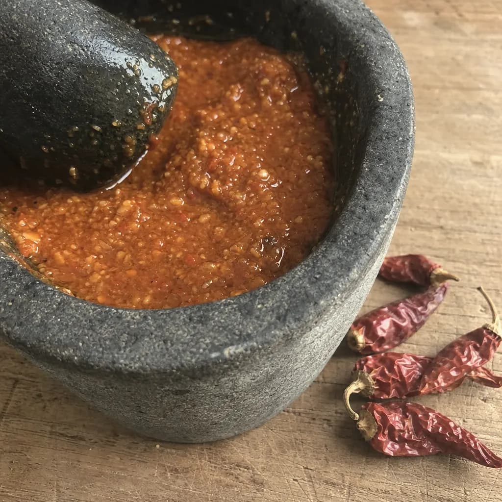 Grainy red mojo in a stone mortar beside dried palmera chillies