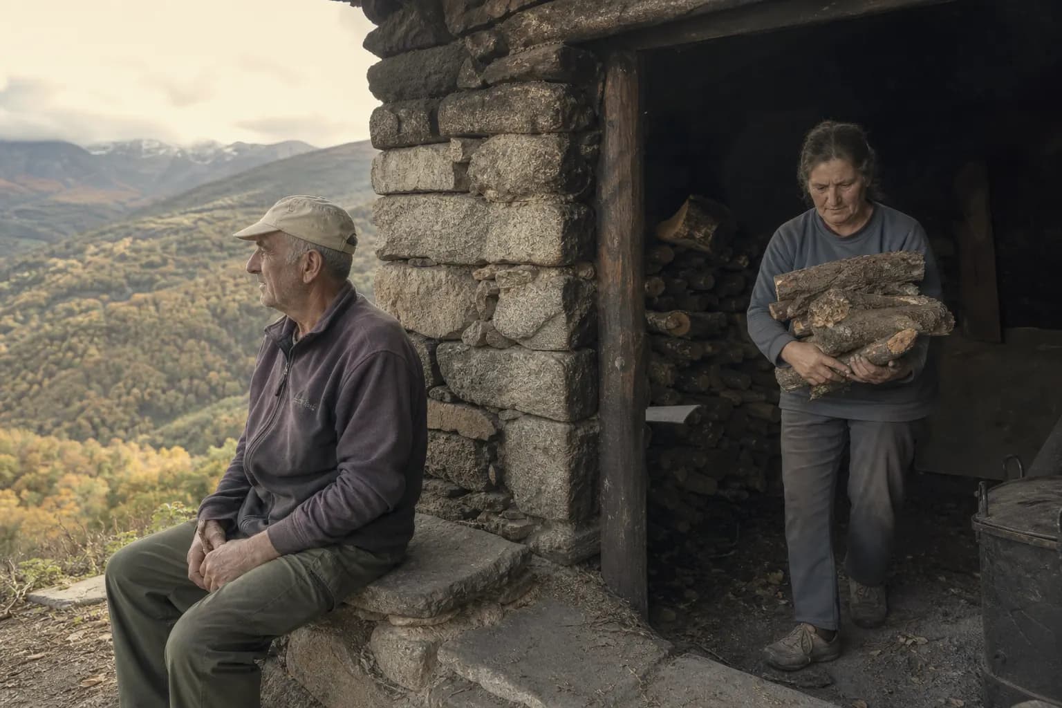Celestino Tovar looks at the valley as Marisa carries oak logs into the smoking house