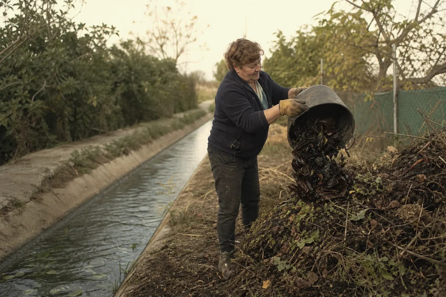 Pili Echarri tips pepper skins onto the compost beside the irrigation channel