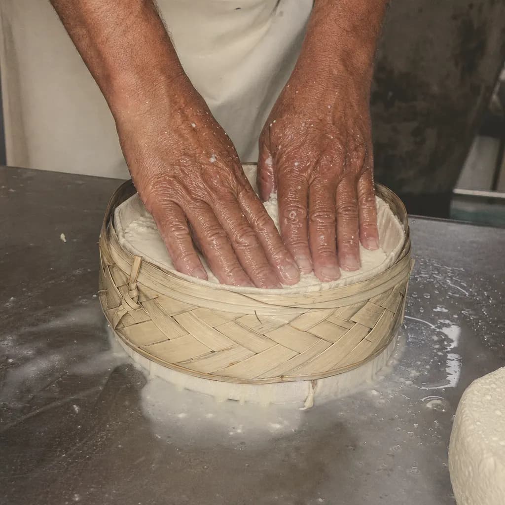 Hands press the curd into a mould with a woven palm band
