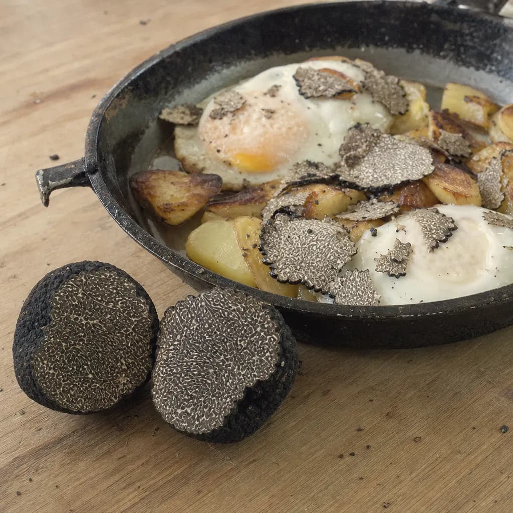 Halved black truffle beside fried eggs and potatoes with grated truffle