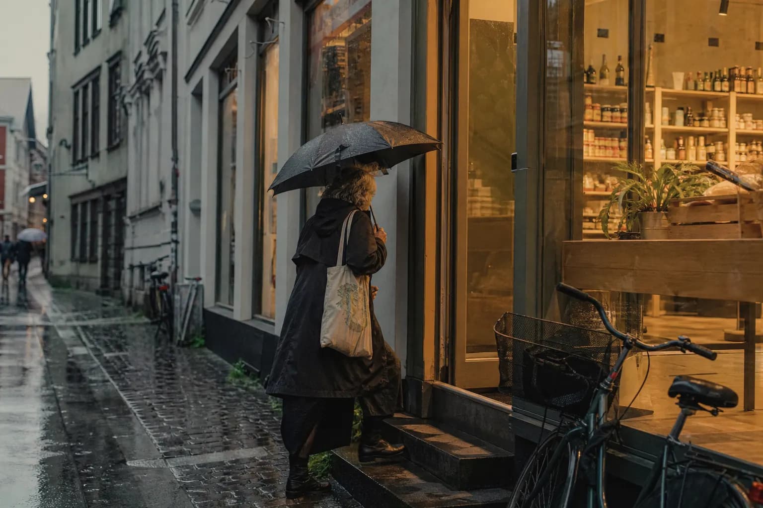 A woman with an umbrella walks into a neighbourhood shop in the rain