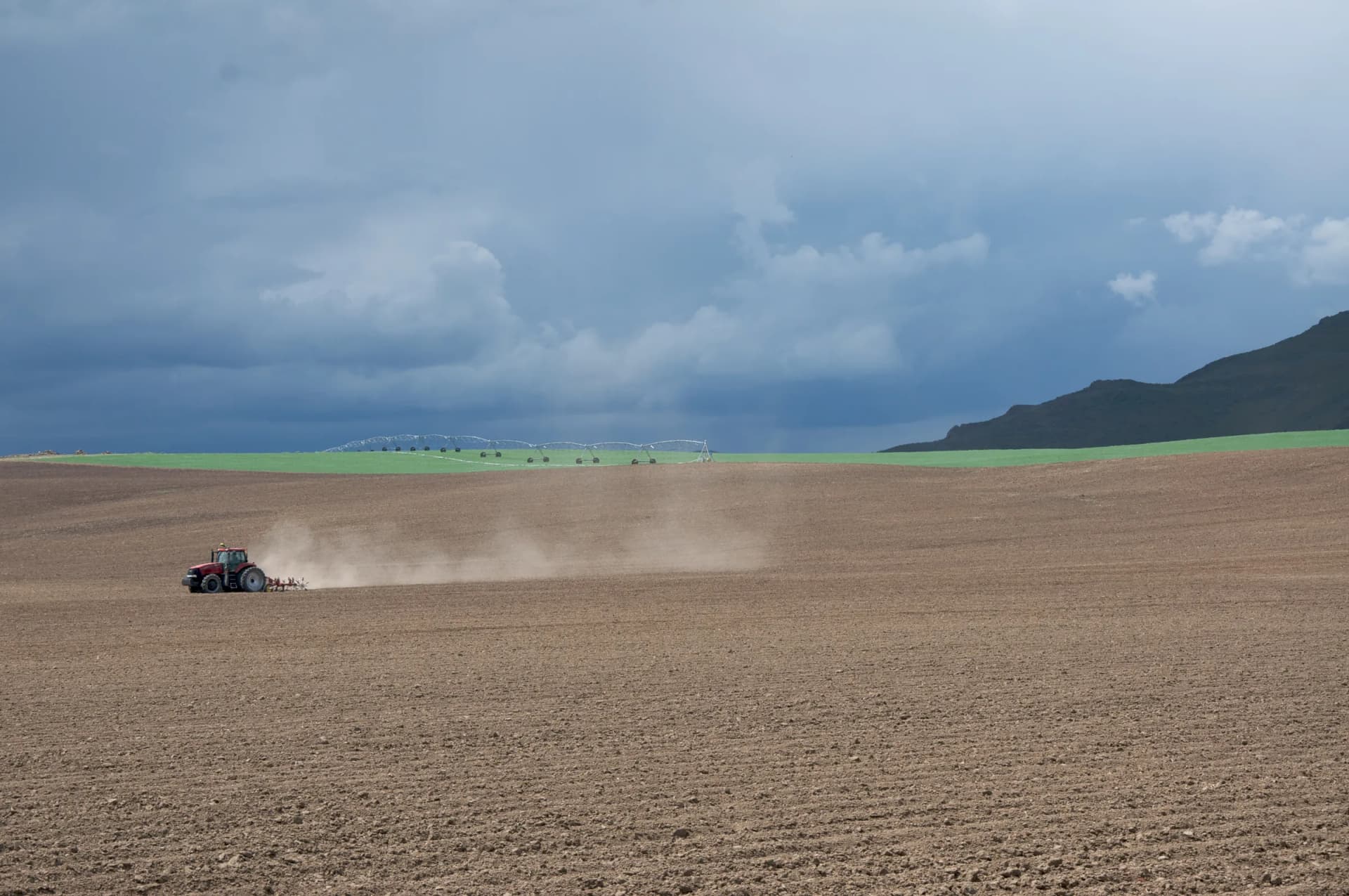 Un tractor labra un campo abierto bajo un cielo de tormenta