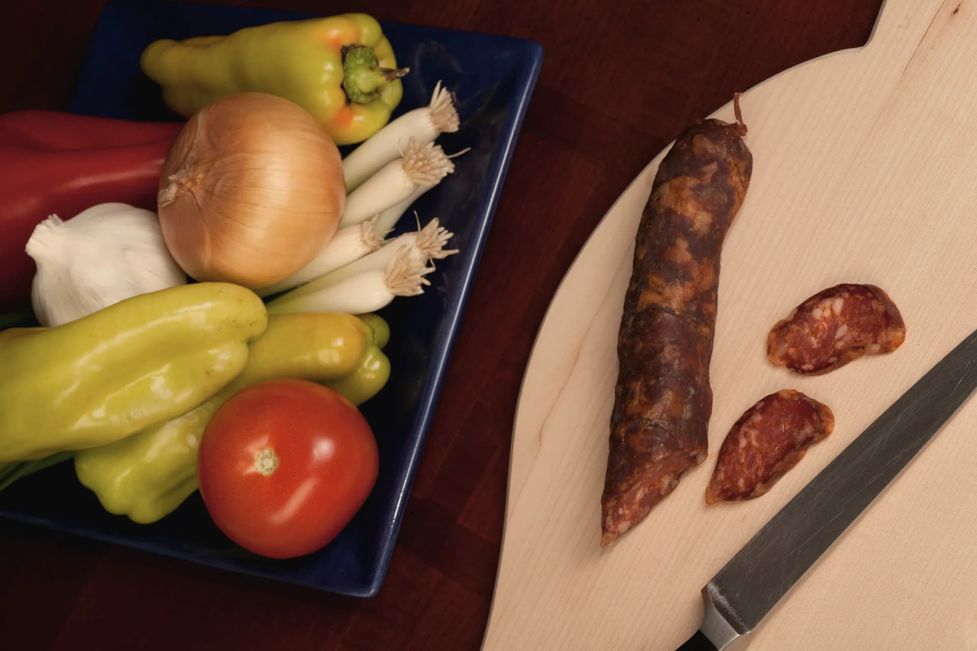 Cured chorizo sliced on a board next to peppers and onion