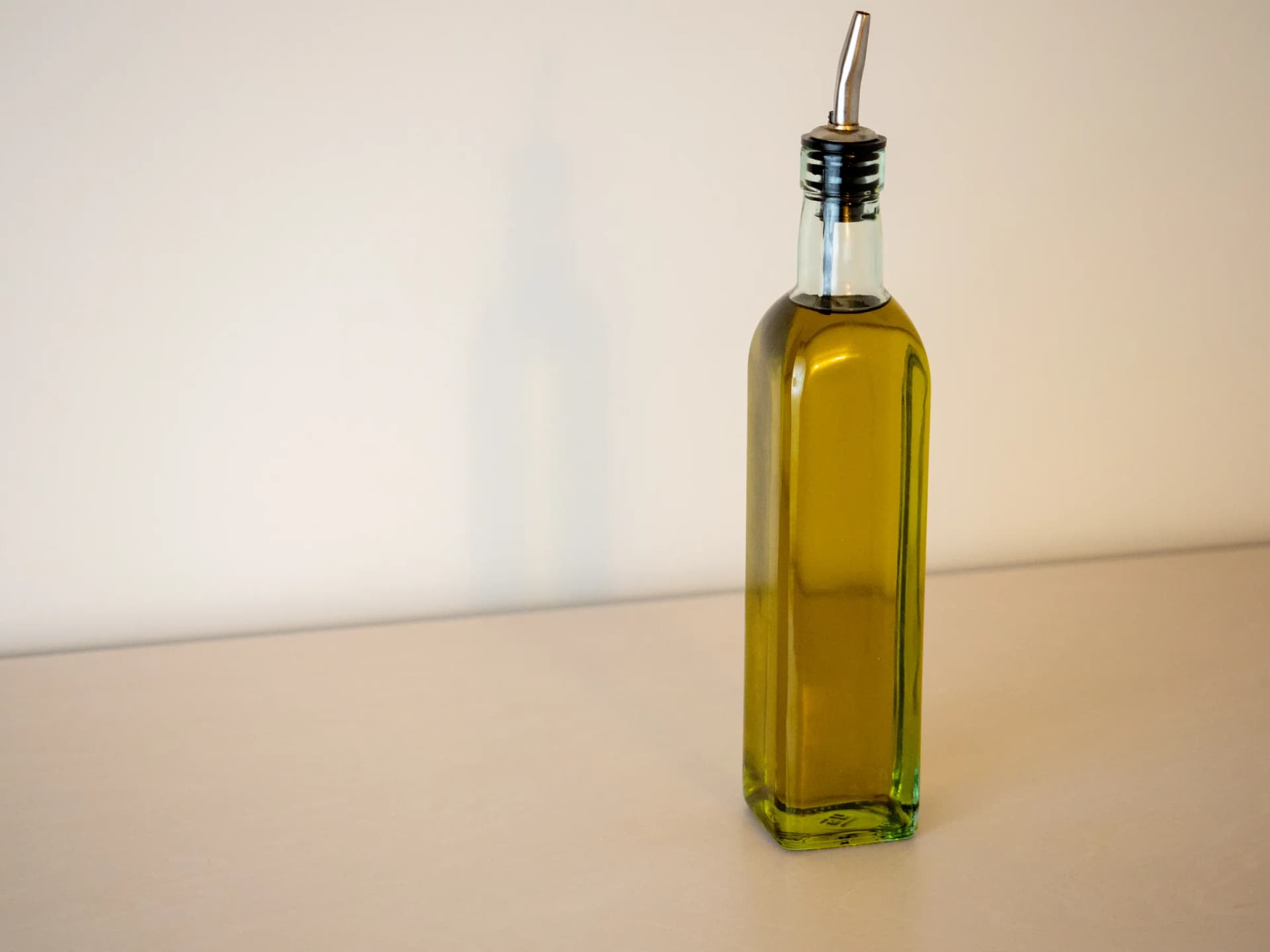 A tall square bottle of olive oil on a plain background