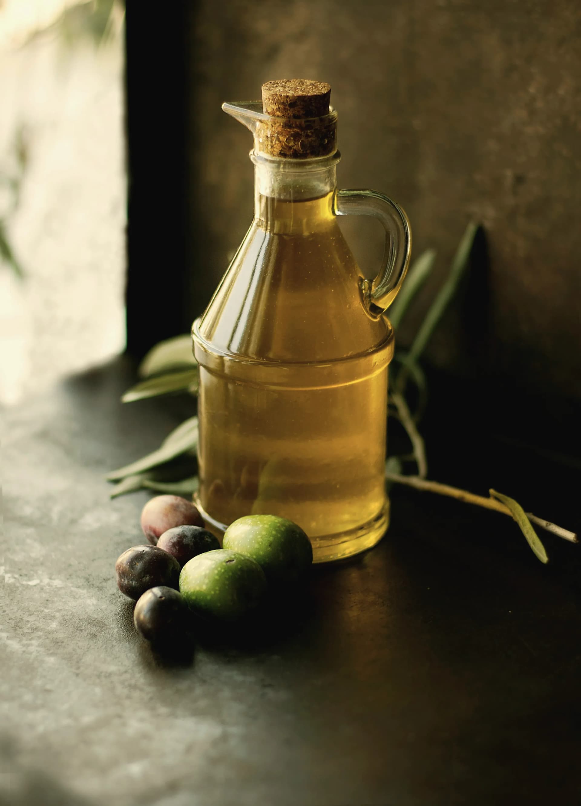 A glass jug full of oil with a few olives