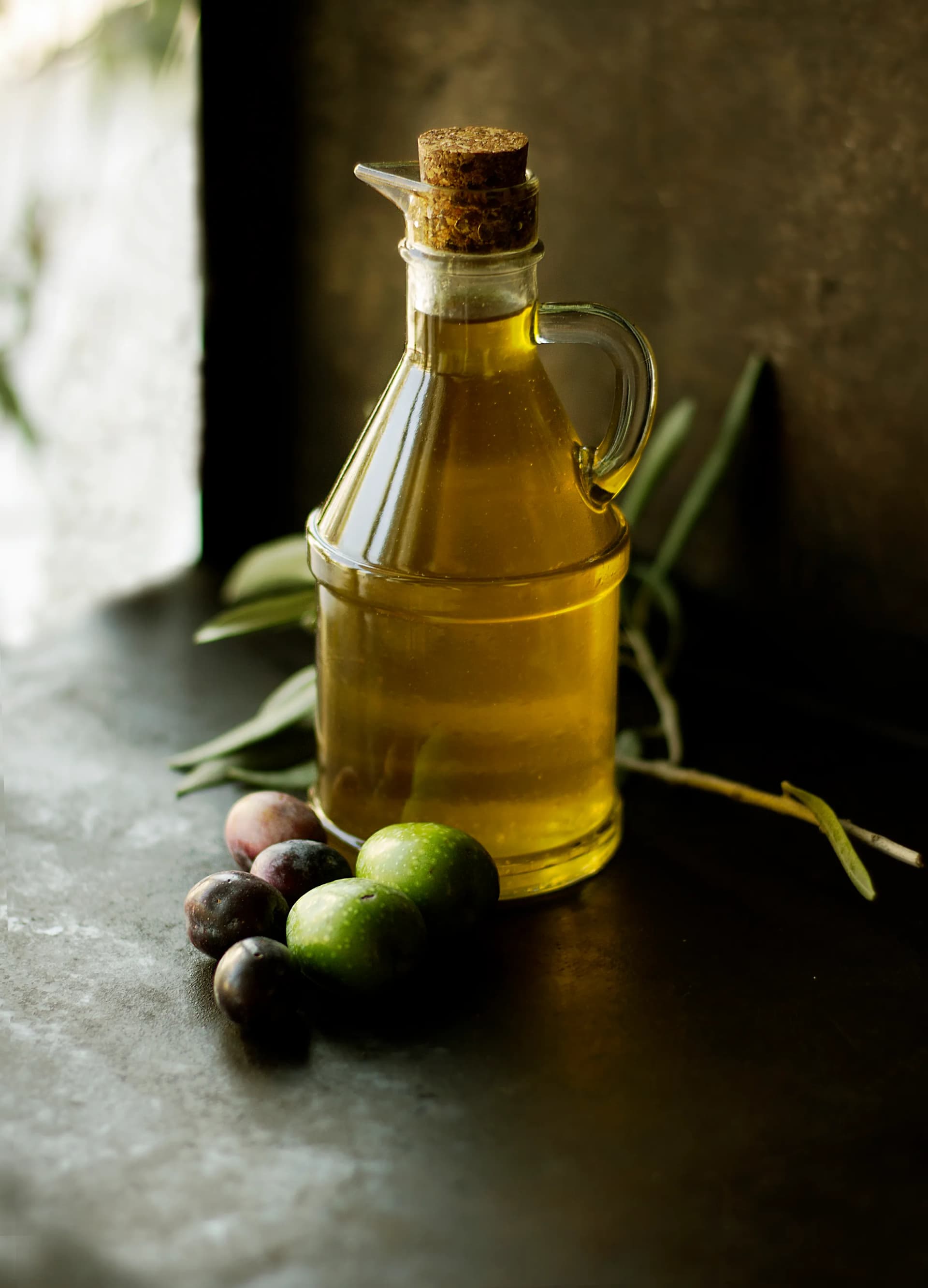 A glass cruet full of green oil beside a few olives